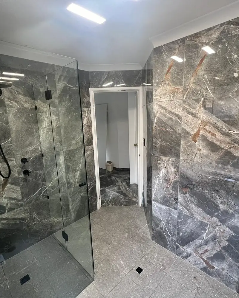 Bathroom renovated in dark marble-look tiles with a frameless glass shower