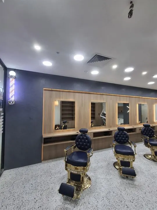Row of barber chairs in front of timber-framed mirrors on a white terrazzo-look floor