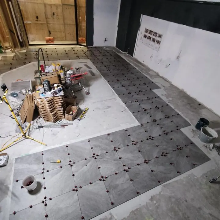 Large-format grey floor tiles going down around a darker inset, with levelling clips on every joint