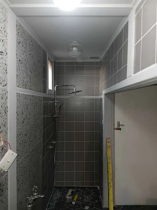 Shower in small grey square tiles beside a terrazzo-look feature wall