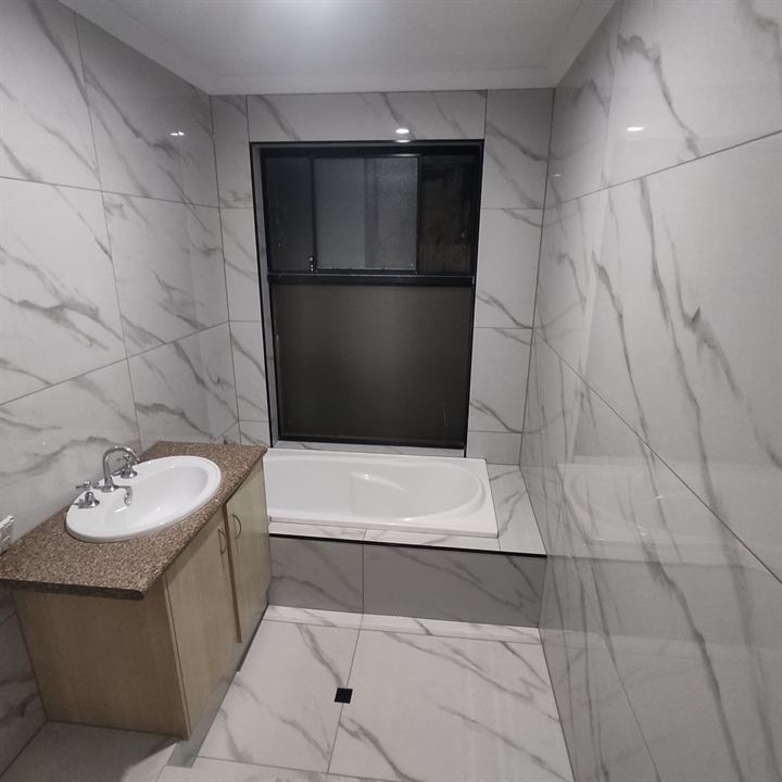 Bathroom in marble-look tiles with a tiled bath hob and vanity