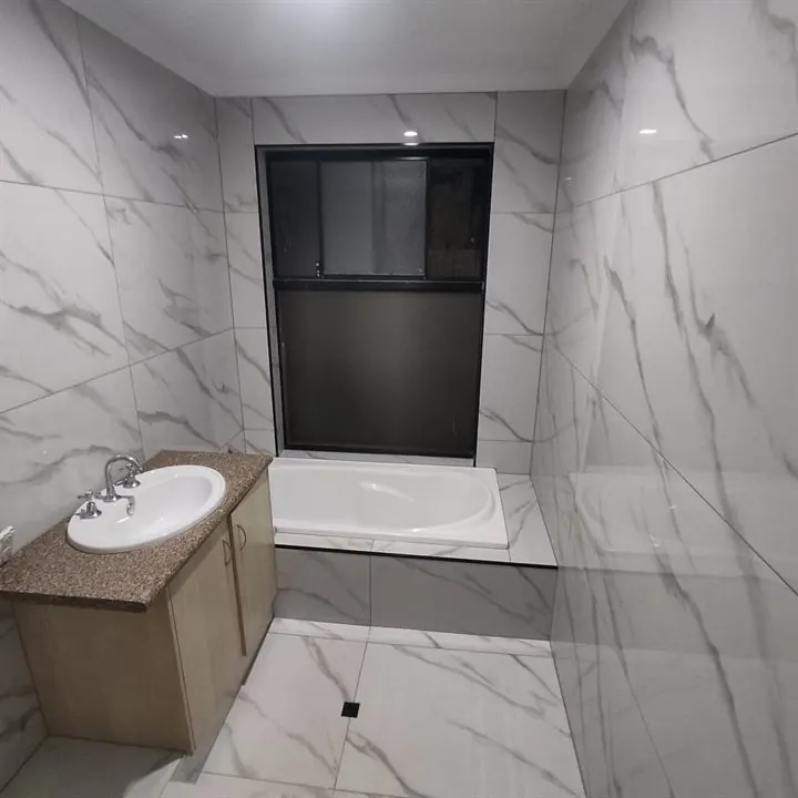 Bathroom in large marble-look tiles with a tiled bath hob