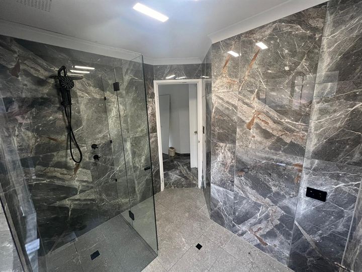 Frameless glass shower in dark marble-look tiles, looking to the doorway