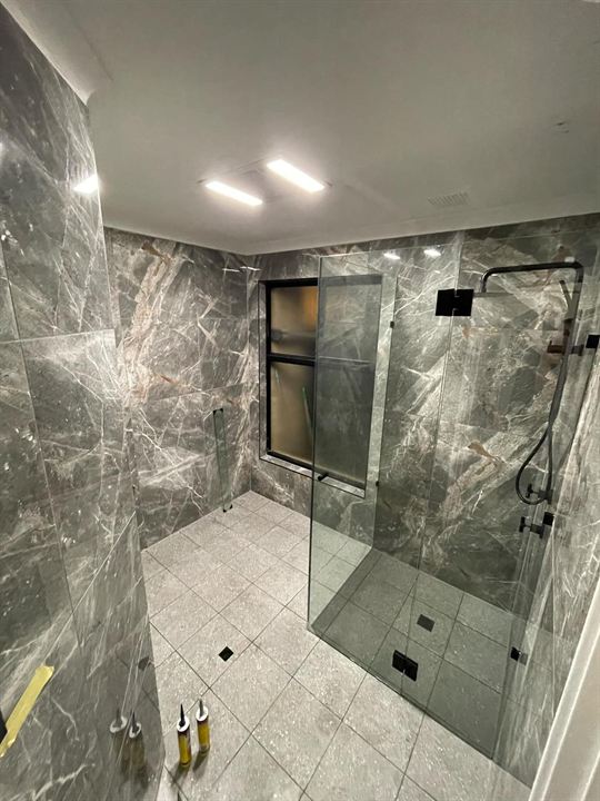 Bathroom in dark marble-look tiles with a frameless glass shower