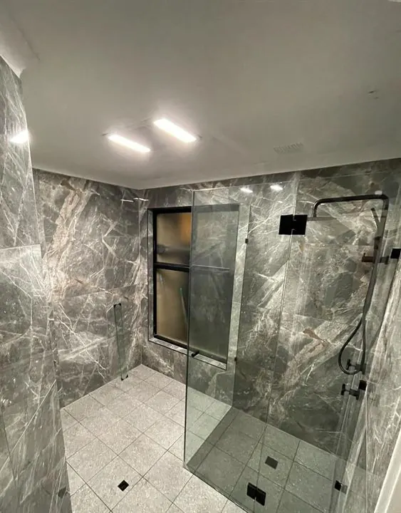 The same bathroom finished in dark marble-look tiles with a frameless shower