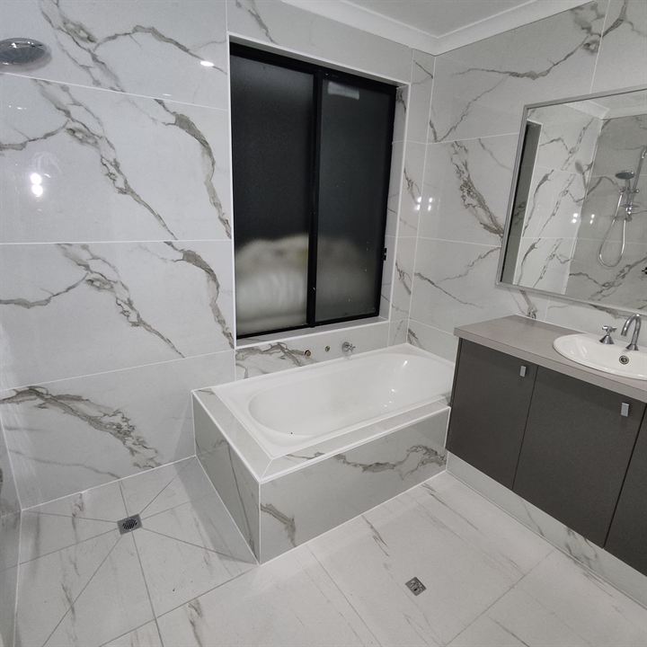 Bathroom tiled in white marble-look tiles, with a tiled bath hob, dark vanity and window
