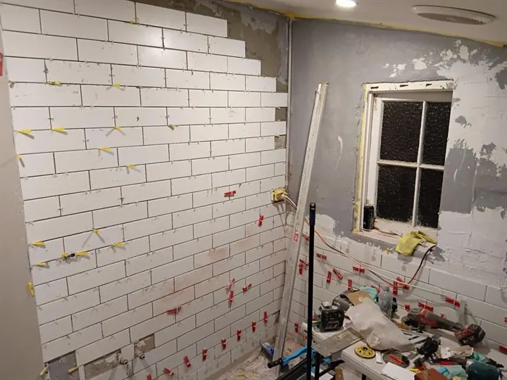 White subway tiles going up a wall in a brick bond, with levelling clips