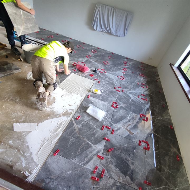 Tiler laying dark marble-look floor tiles with levelling clips