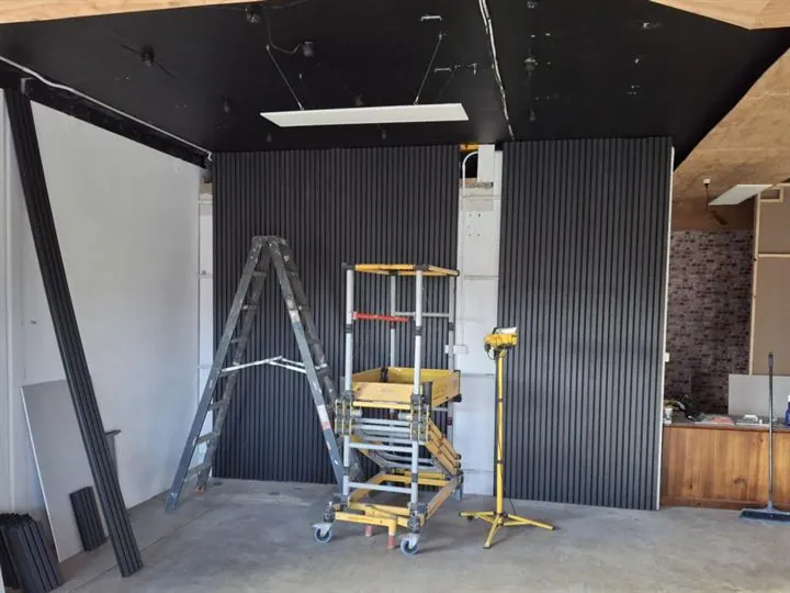 Black batten cladding being fixed to a feature wall, with a mobile scaffold in front