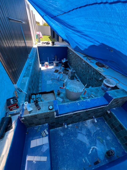 Pool being tiled in green tiles over a blue waterproofing membrane
